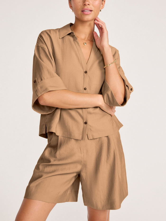 Woman wearing a camel oversized button-up shirt with matching pleated bermuda shorts