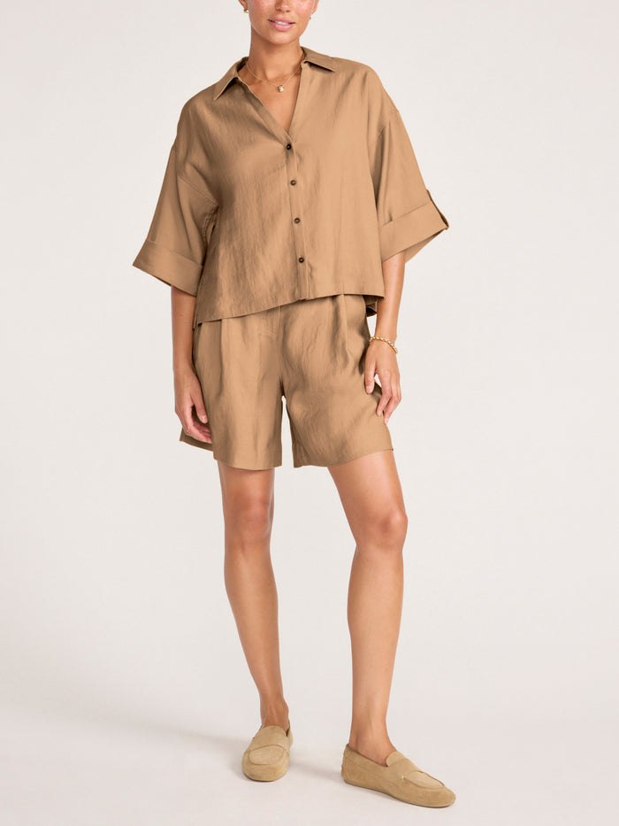 Full-length view of a woman wearing a camel oversized button-up shirt and matching bermuda shorts with suede loafers