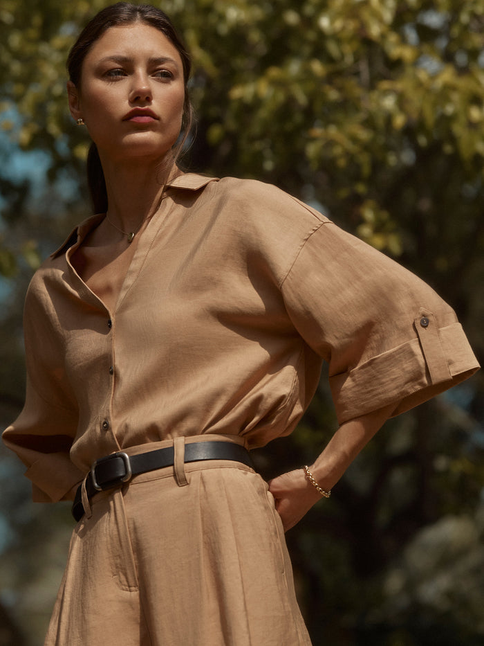 Close-up of a woman wearing a camel button-down shirt with a black belt, outdoors