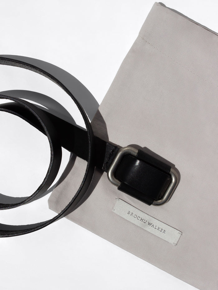 Coiled black leather belt with a dark buckle resting on a Brochu Walker branded dust bag