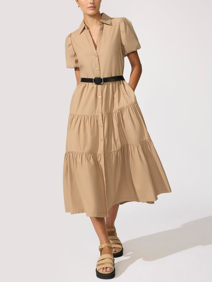 Woman wearing a beige tiered shirtdress with a black belt and platform sandals against a white background