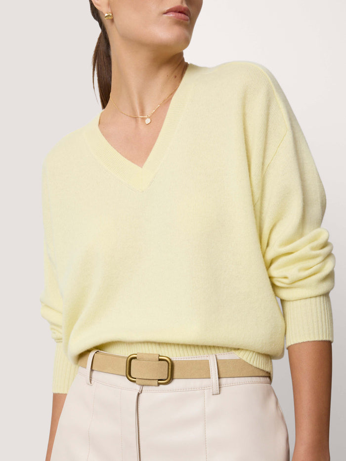 Woman wearing a pale yellow oversized V-neck sweater with cream trousers and a tan leather belt