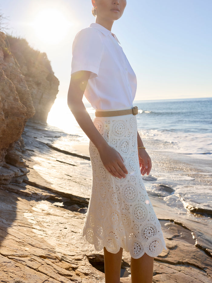 Woman in a white polo top and eyelet lace midi skirt on a rocky beach