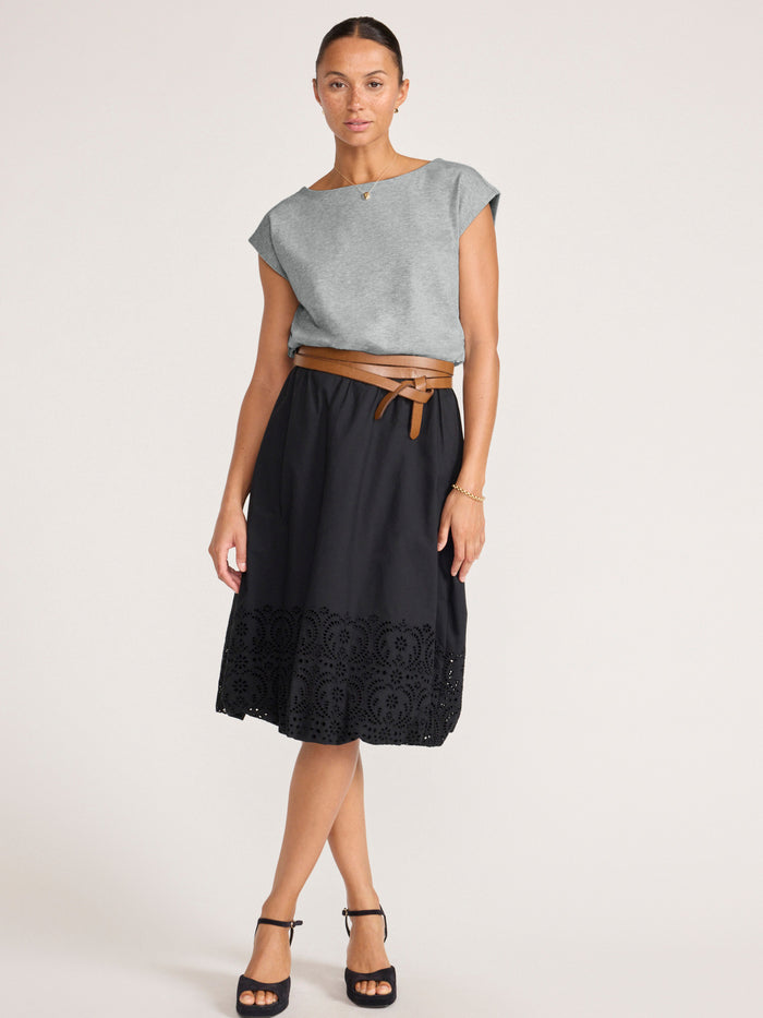 Woman wearing a pebble grey top with a tan wrap belt over a black eyelet skirt, full-length front view