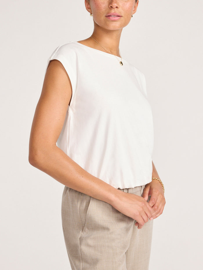 Model wearing a white cap-sleeve crew neck top with beige trousers