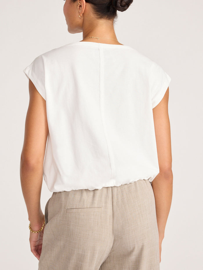 Back view of a model wearing a white cap-sleeve top with beige trousers