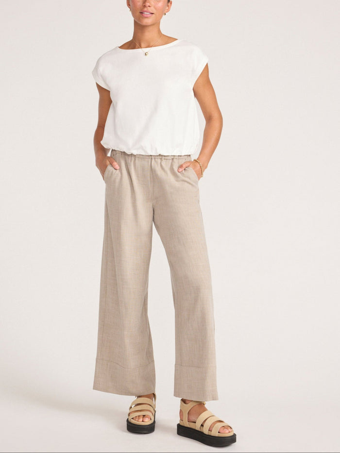 Full-length view of a model in a white cap-sleeve top with wide-leg beige trousers and sandals